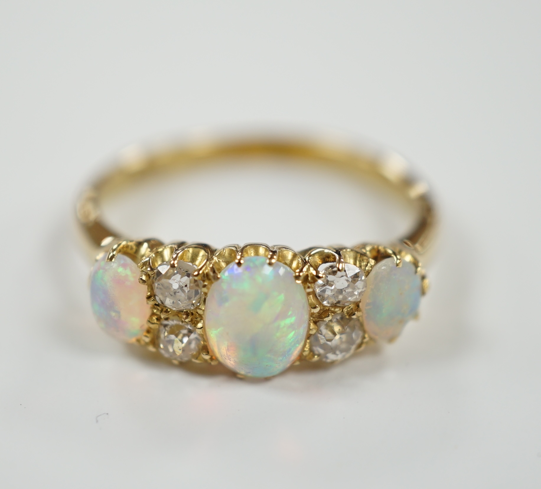 A yellow metal (tests as 18ct), three stone white opal and four stone diamond set half hoop ring, size N/O, gross weight 3.5 grams.